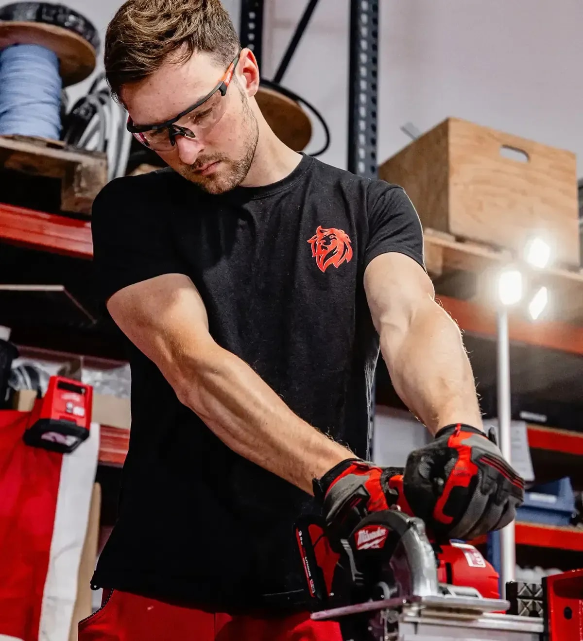Handwerker mit Schutzbrille sägt konzentriert mit Akku-Handkreissäge in der Werkstatt