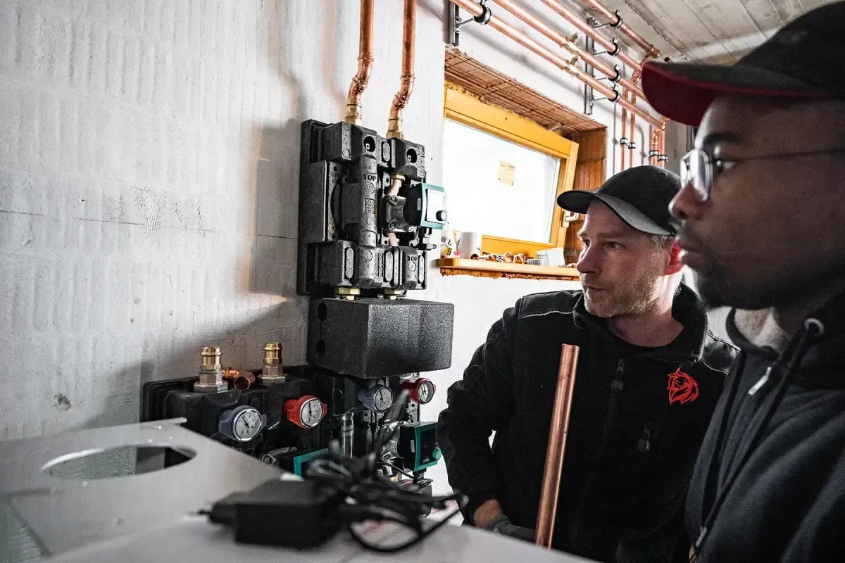 Zwei Heizungsmonteure prüfen eine Heizungsanlage mit Pumpen und Verteiler im Heizraum